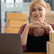 Mulher sentada em frente ao computador, olhando para frente e dando um sorriso