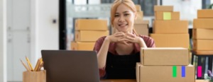 Mulher sentada em frente ao computador, olhando para frente e dando um sorriso