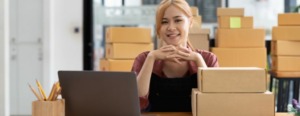 Mulher sentada em frente ao computador, olhando para frente e dando um sorriso