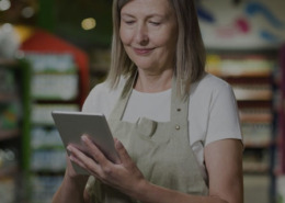 Imagem de uma mulher em um supermercado olhando para o tablet que está em sua mão