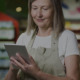 Imagem de uma mulher em um supermercado olhando para o tablet que está em sua mão