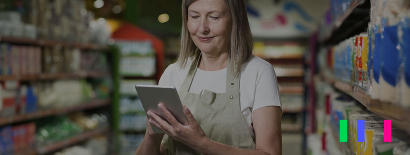 Imagem de uma mulher em um supermercado olhando para o tablet que está em sua mão