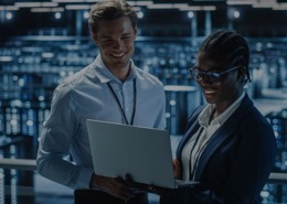 Imagem de um homem e mulher conversando com um notebook na mão em um ambiente empresarial