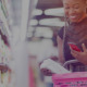 Foto de mulher no supermercado com uma cesta cheia de produtos e um celular na mão