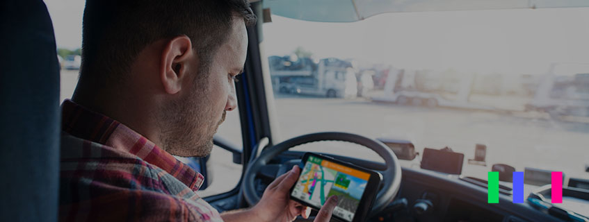 Homem dentro de um caminhao, em frente ao volante, visualizando a rota no celular