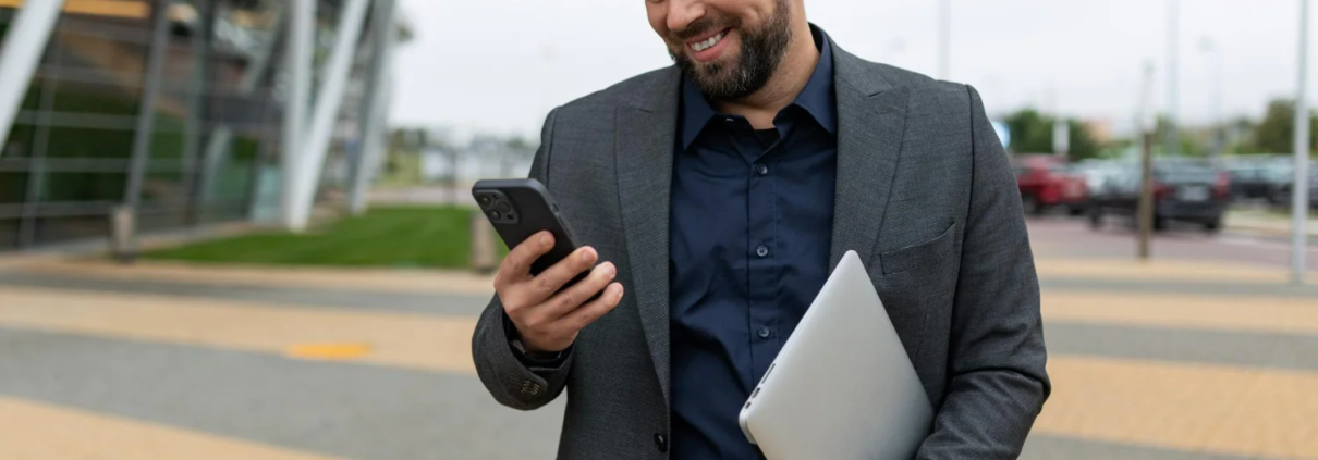 Representante comercial sorrindo na rua e usando aplicativo de vendas no celular, ilustrando o controle da força de vendas.