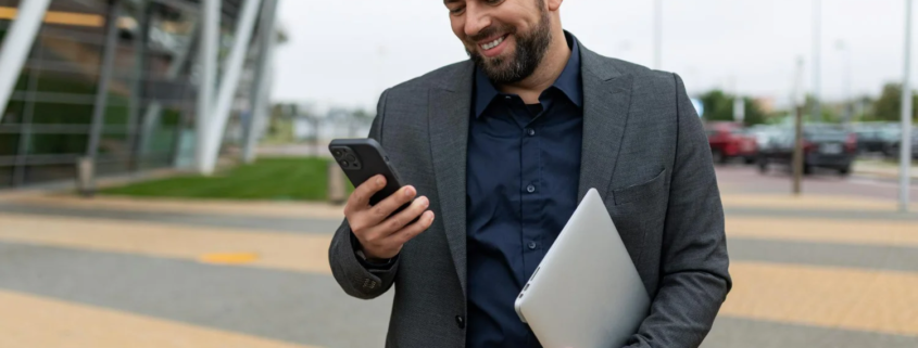 Representante comercial sorrindo na rua e usando aplicativo de vendas no celular, ilustrando o controle da força de vendas.